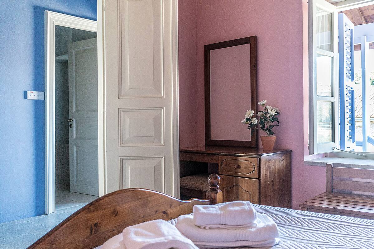 Ein Schlafzimmer mit einem hölzernen Bett, einem Schminktisch, einem Spiegel und einem Fenster mit Blick nach draußen.