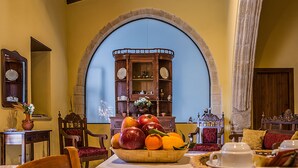 A dining area with a table set for tea, a fruit bowl, and a wooden cabinet with a mirror and decorative items.