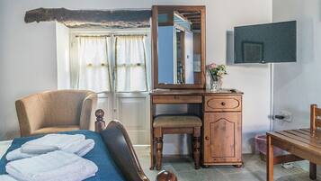 Un dormitorio con cama, un escritorio de madera, una silla, un televisor y una ventana con cortinas.