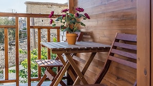 A wooden deck with a table and chairs, a potted plant with flowers, and a stone wall in the background.
