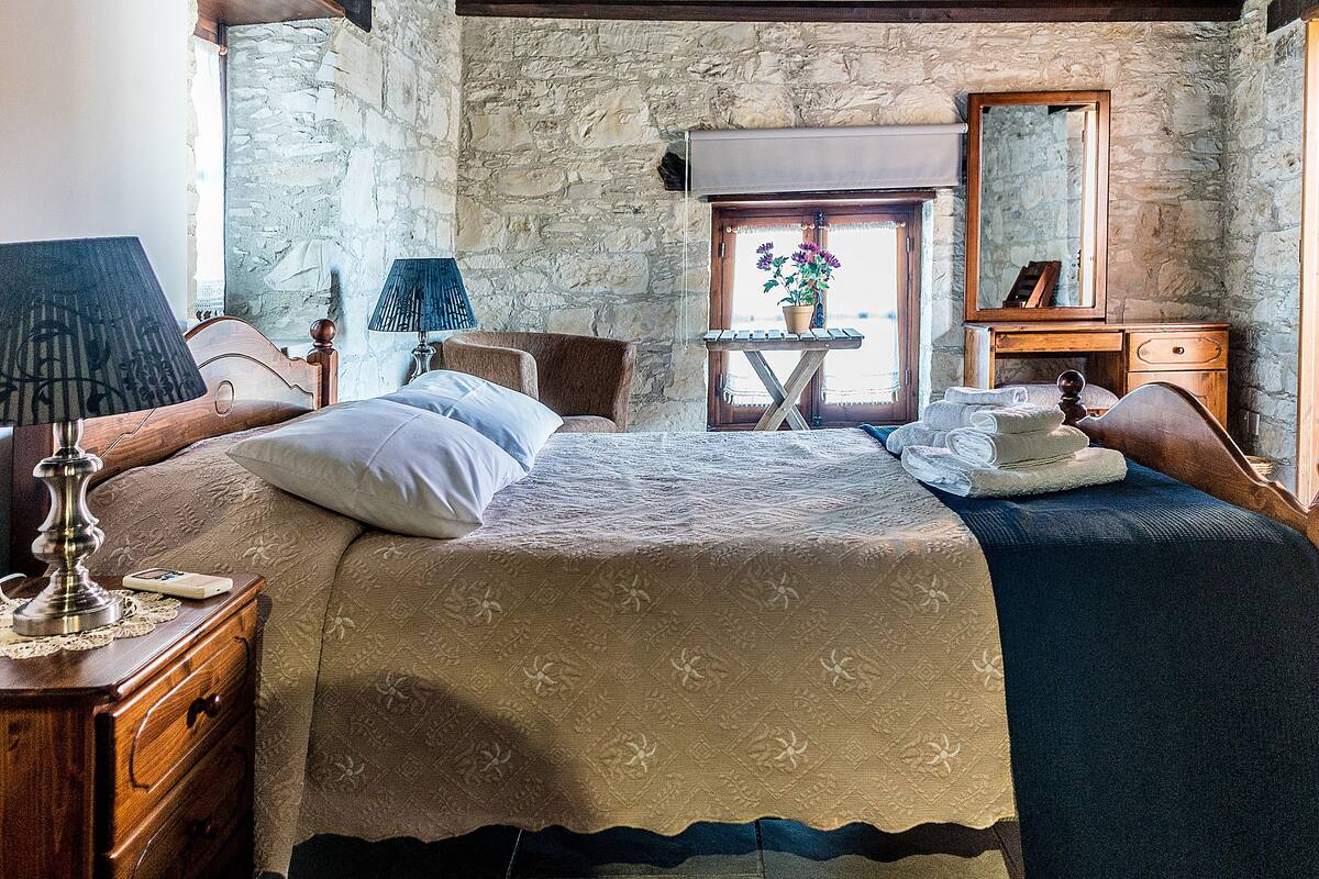 Ein Schlafzimmer mit Stehwänden, einem hölzernen Bett, einem Nachttisch, einer Kommode, einem Spiegel und einem Fenster mit Blick.
