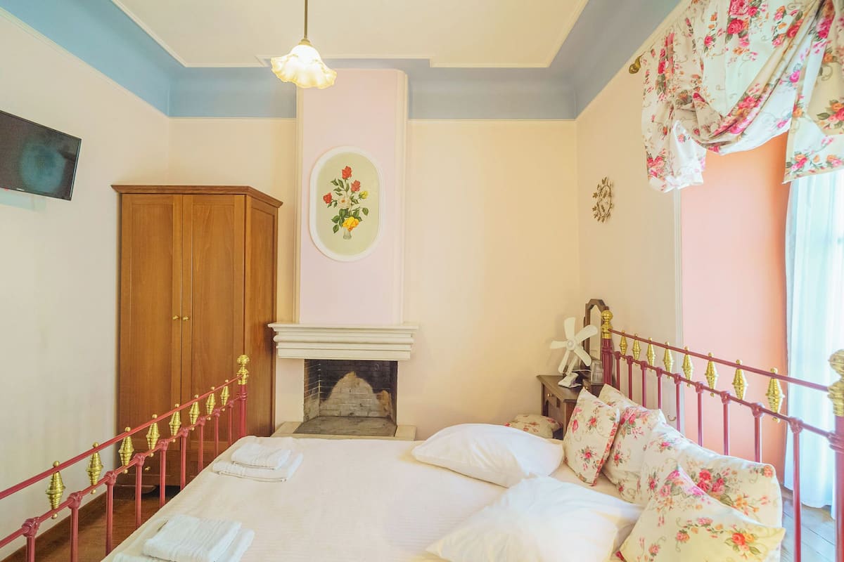 A bedroom with a bed, a wooden wardrobe, a fireplace, and a nightstand.