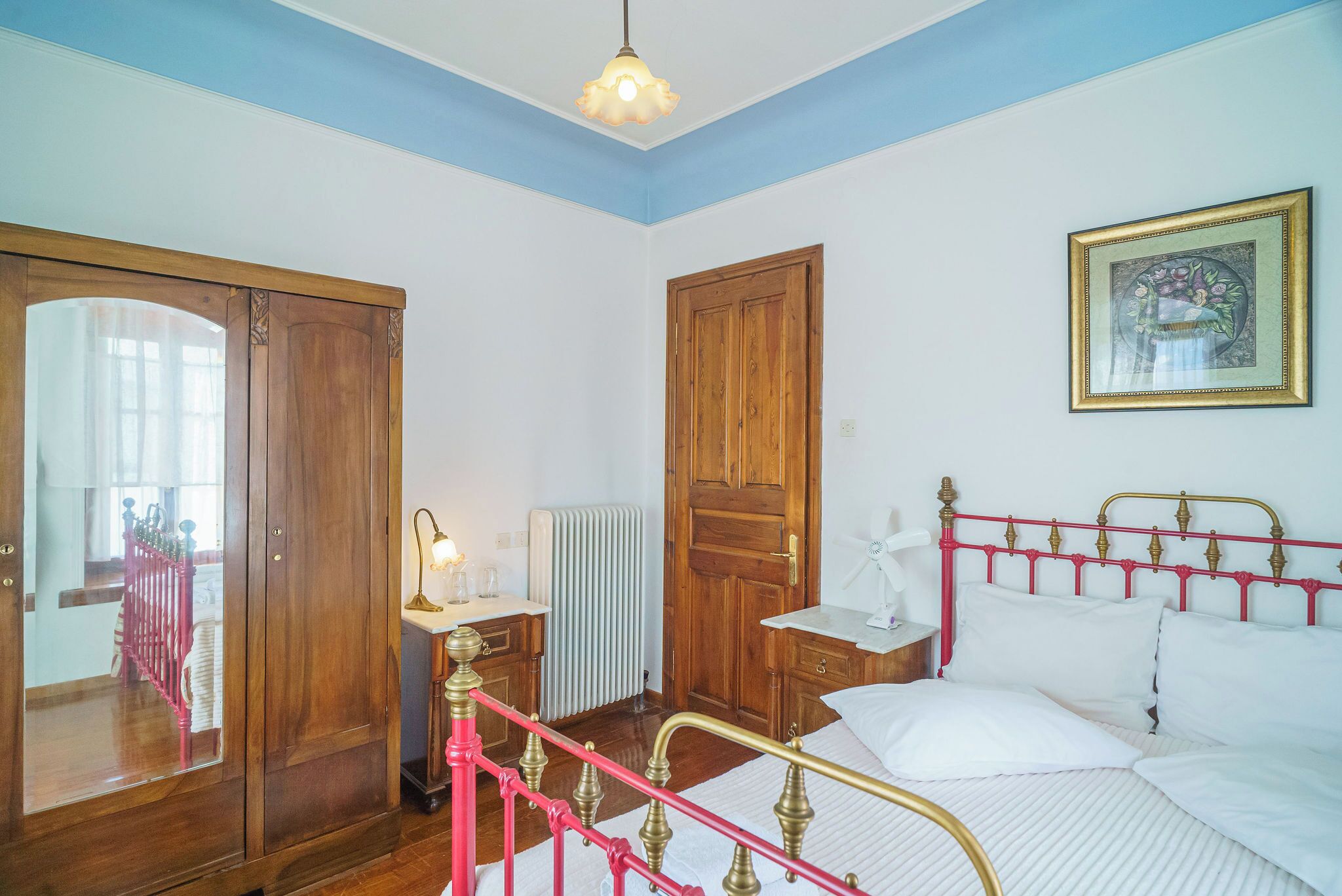 A bedroom with a bed, a wooden wardrobe, a radiator, and a framed picture on the wall.