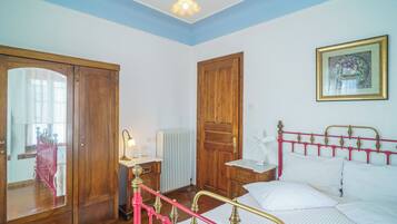 A bedroom with a bed, a wooden wardrobe, a radiator, and a framed picture on the wall.