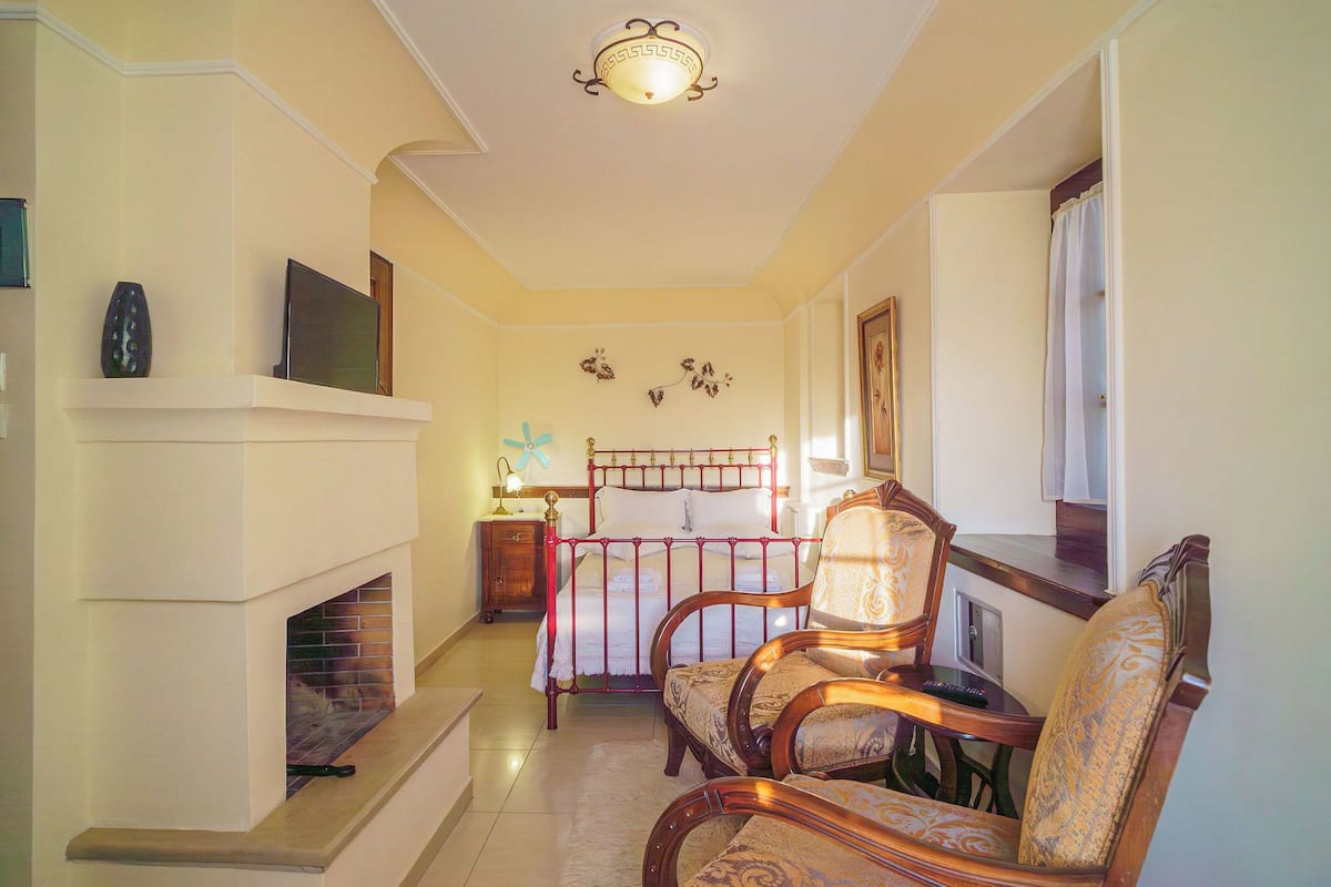A bedroom with a bed, two chairs, a nightstand, a lamp, and a fireplace.