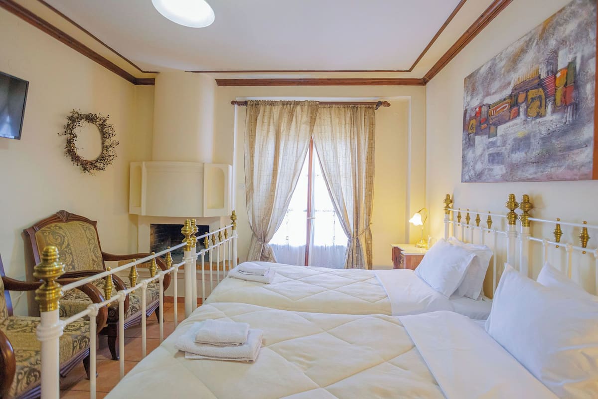 A hotel room with a large bed, a chair, a fireplace, and a painting on the wall.