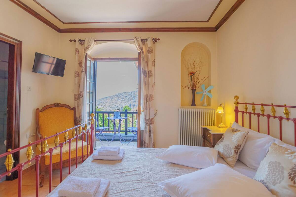 A hotel room with a bed, a TV, a balcony with a view, and a radiator.