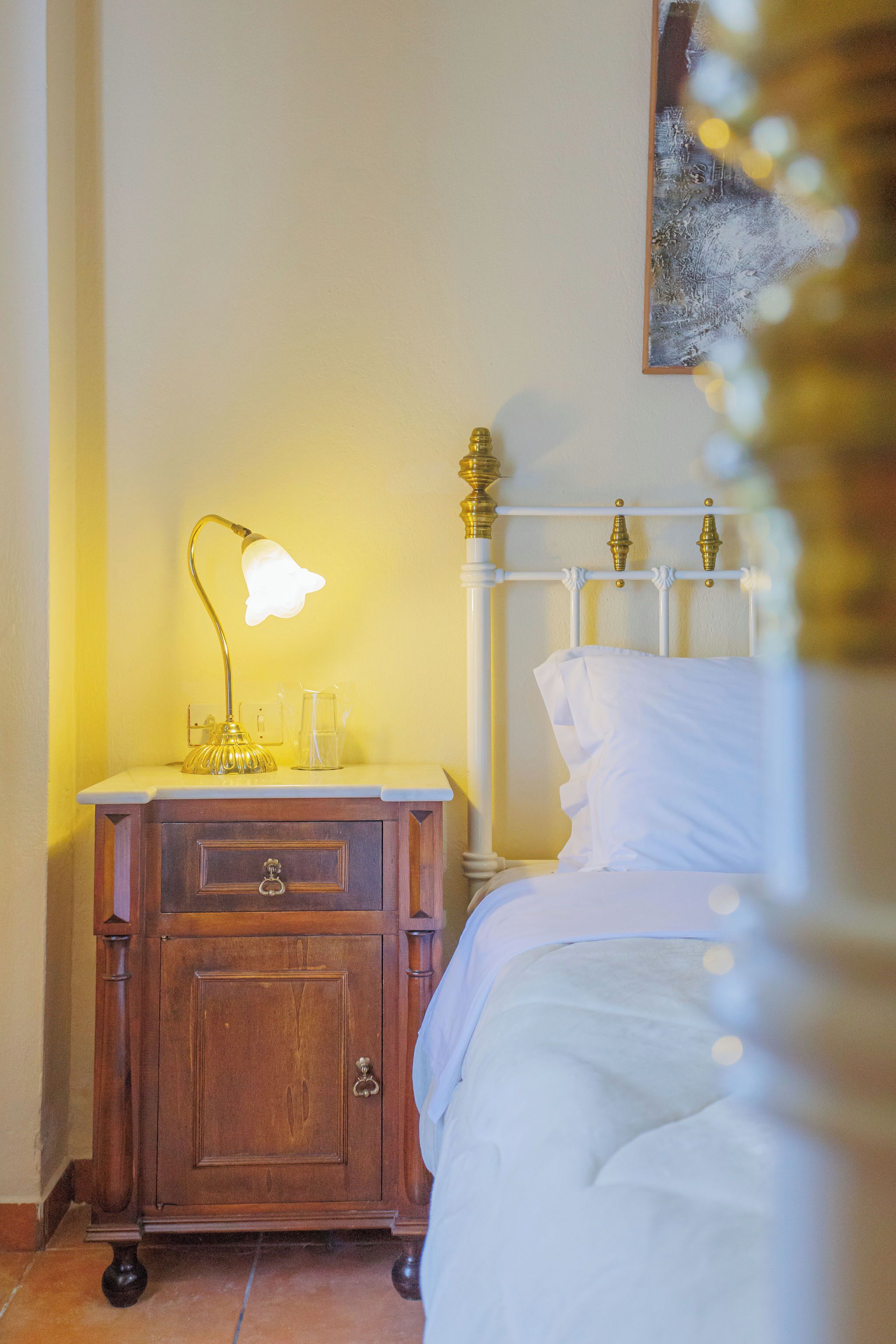Een opgemaakt bed met witte lakens, een nachtkastje met een lamp, en een houten nachtkastje met lades.
