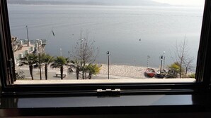 A view of a calm sea from a window overlooking a beach with palm trees and a parked car.