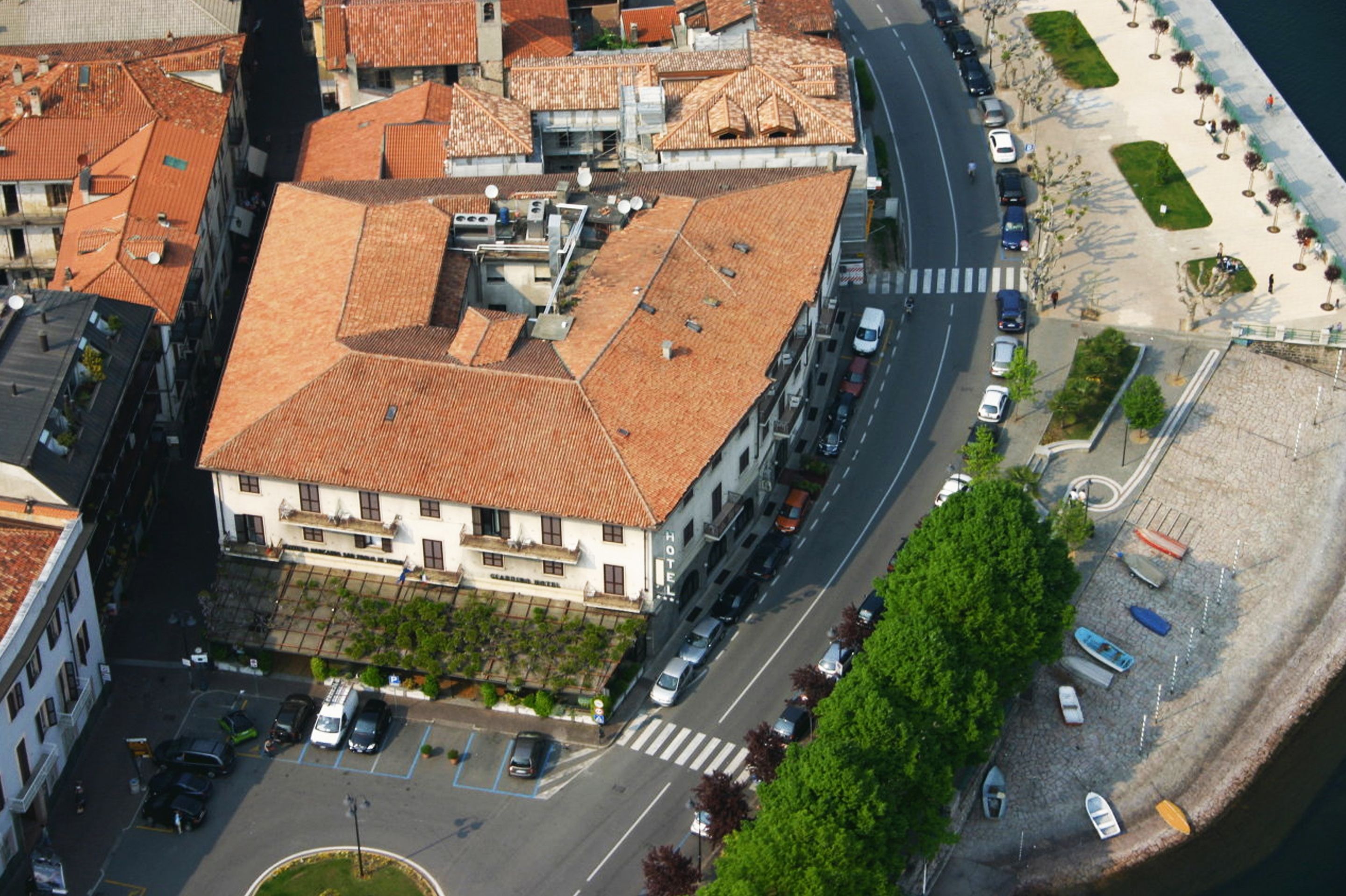 Un hotel con techo de tejas rojas, situado cerca de una orilla con zona de estacionamiento y paseo peatonal.