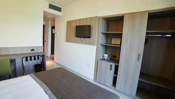 Quarto de hotel com uma cama, uma escrivaninha, uma televisão na parede e um guarda-roupa com prateleiras.