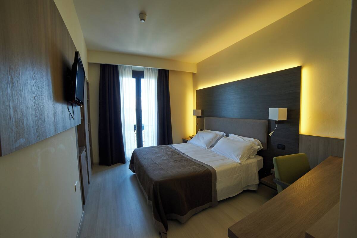 A hotel room with a bed, bedside table, lamp, and a flat-screen TV mounted on the wall.