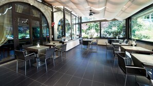 An indoor dining area with tables and chairs, large windows, and a stone wall.