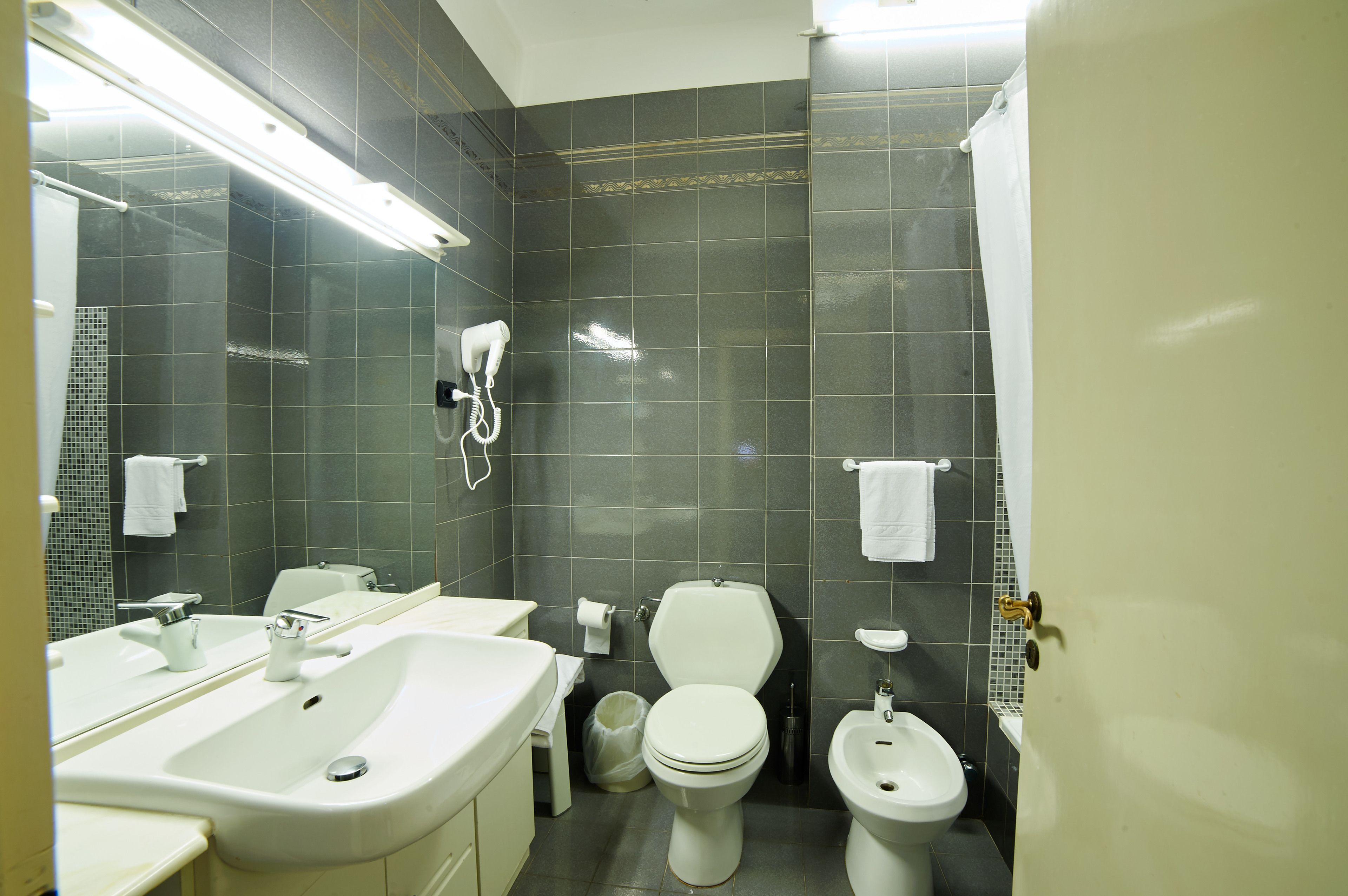 Une salle de bain équipée d’un lavabo, de toilettes, d’un bidet et d’un sèche-cheveux fixé au mur.