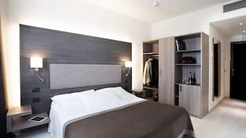 Une chambre d’hôtel moderne dotée d’un grand lit, de tables de chevet, d’une armoire et d’une étagère intégrée où se trouvent une bouteille et des verres.