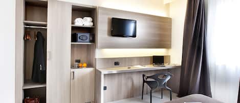 Una habitación de hotel moderna con un armario de madera, un escritorio con una computadora portátil, un televisor y una silla.