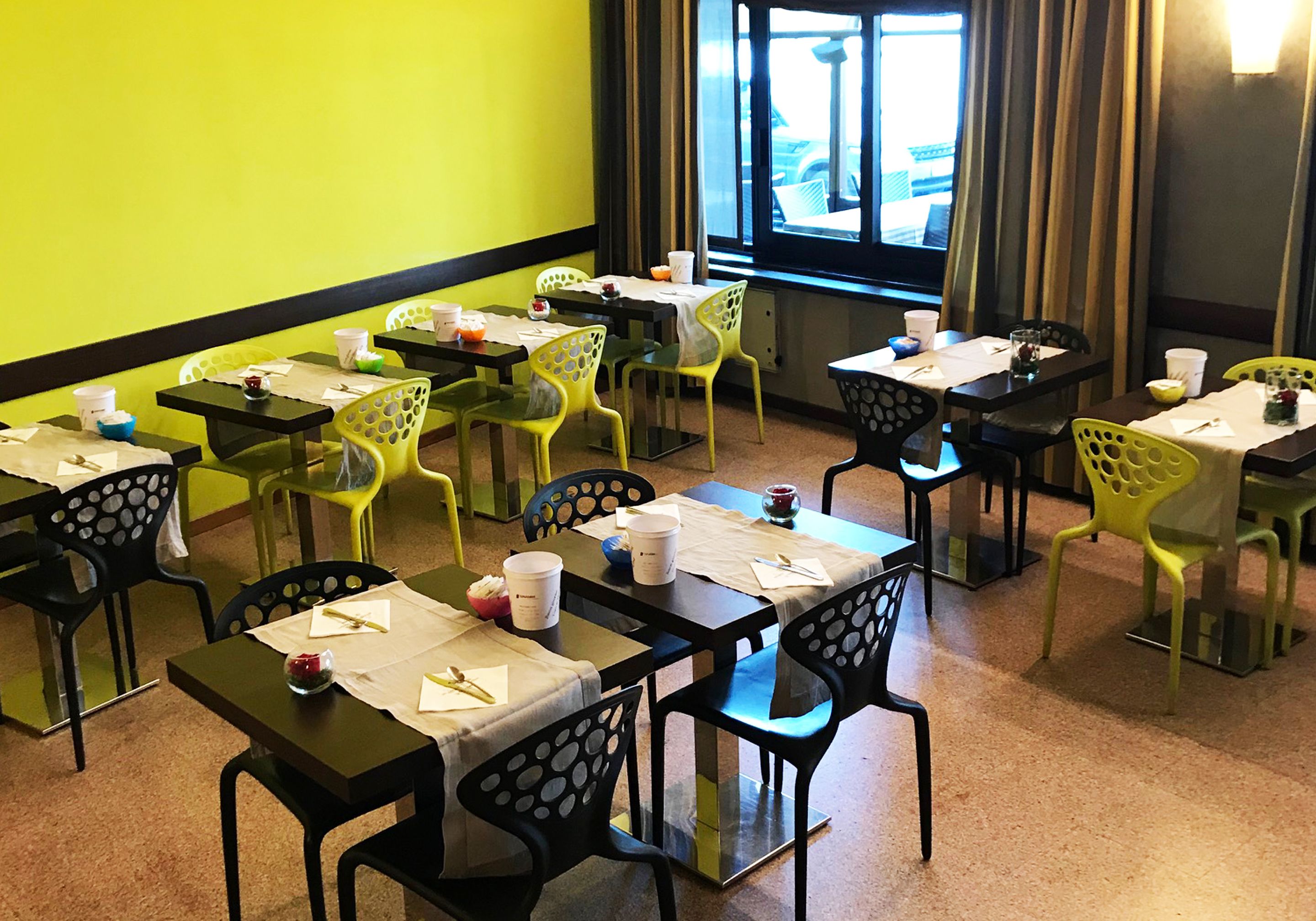 Un comedor con mesas y sillas, algunas con papeles y tazas encima.