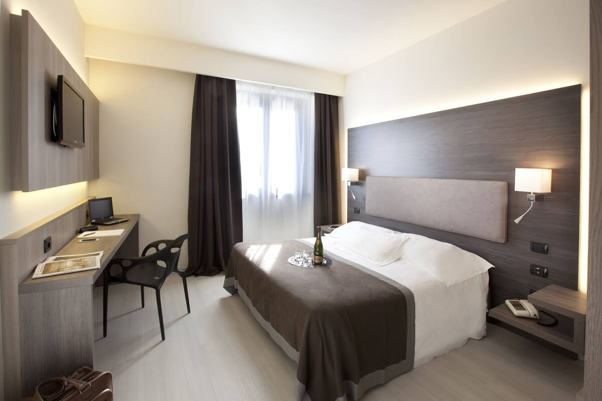 A modern hotel room with a bed, desk, chair, and a TV mounted on the wall.