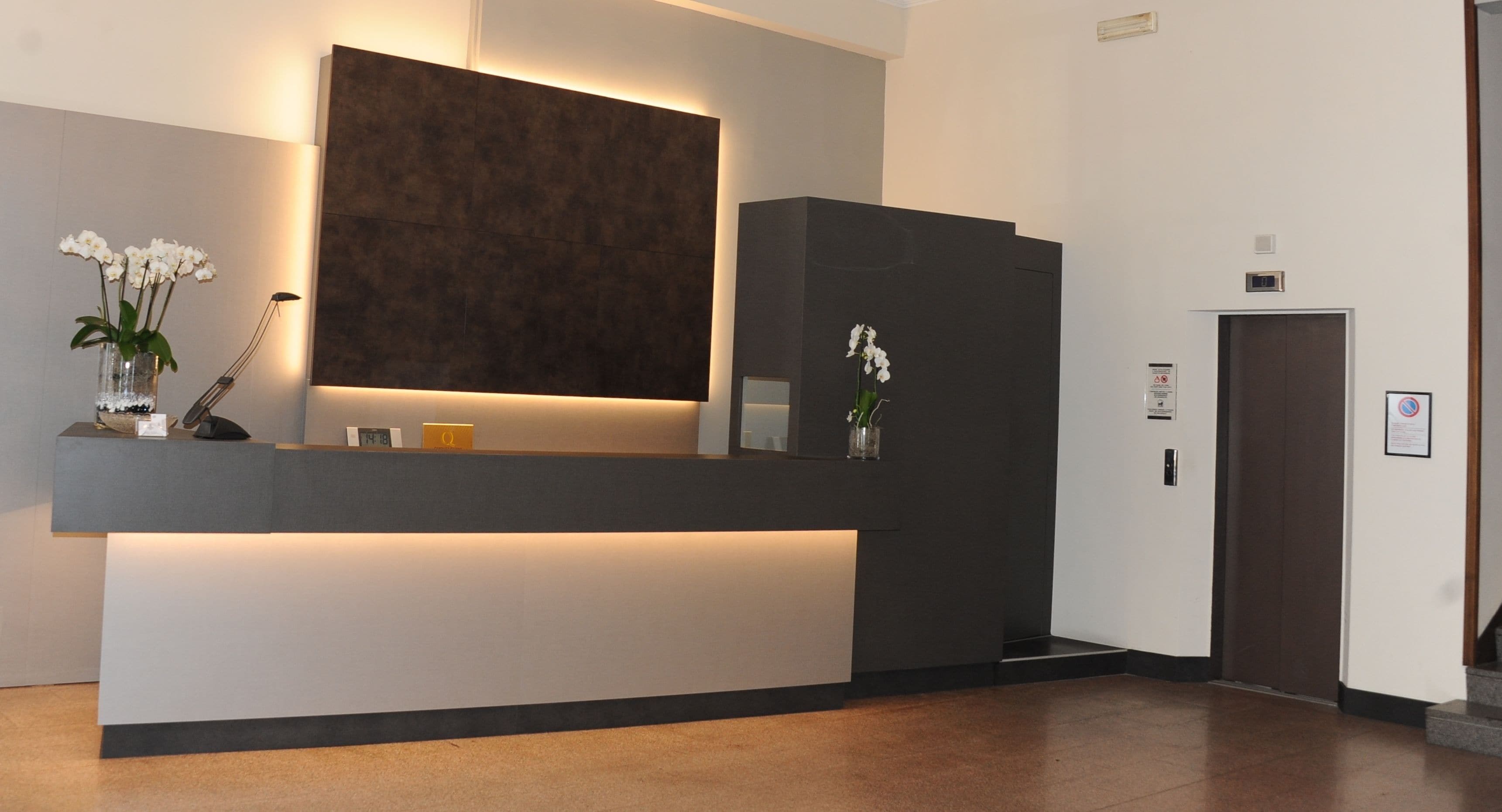 A modern reception desk with a dark panel and a white counter, flanked by two vases with white flowers.
