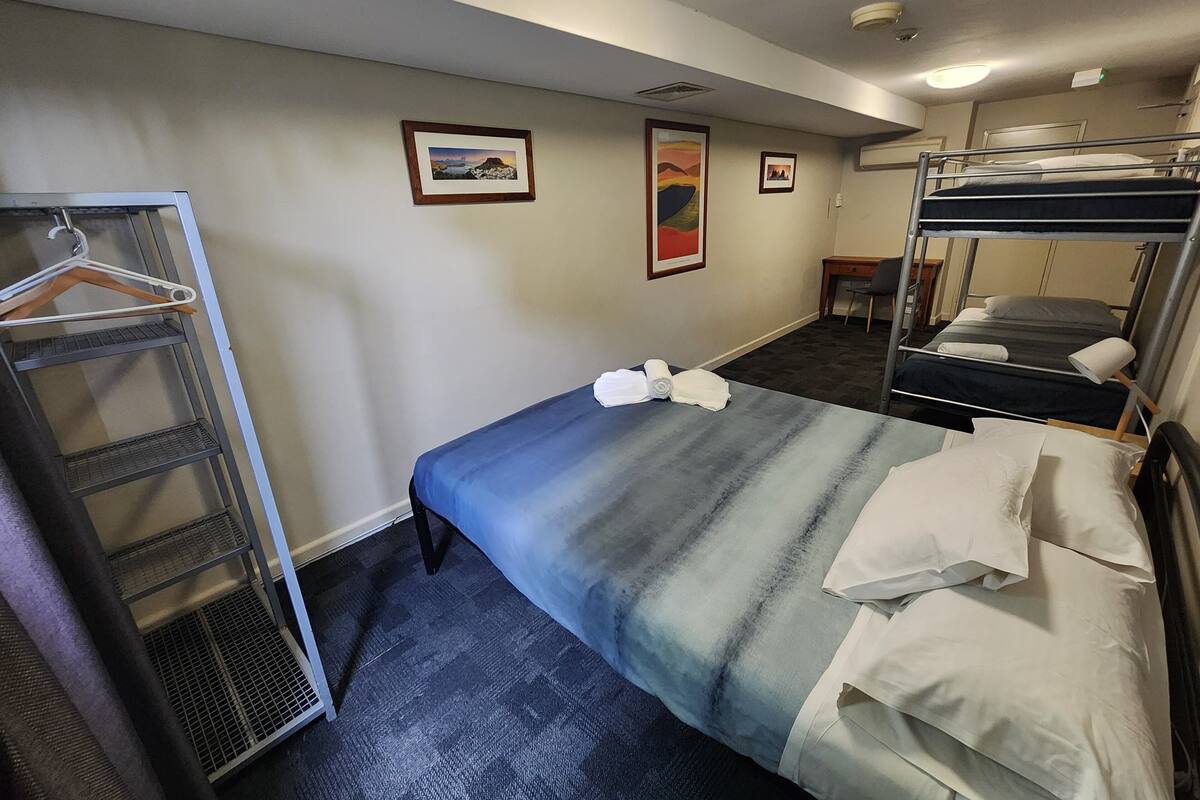 Una habitación de hotel con literas, un perchero y un escritorio pequeño.