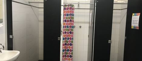 A public restroom with a shower area, a sink, and a tiled floor.