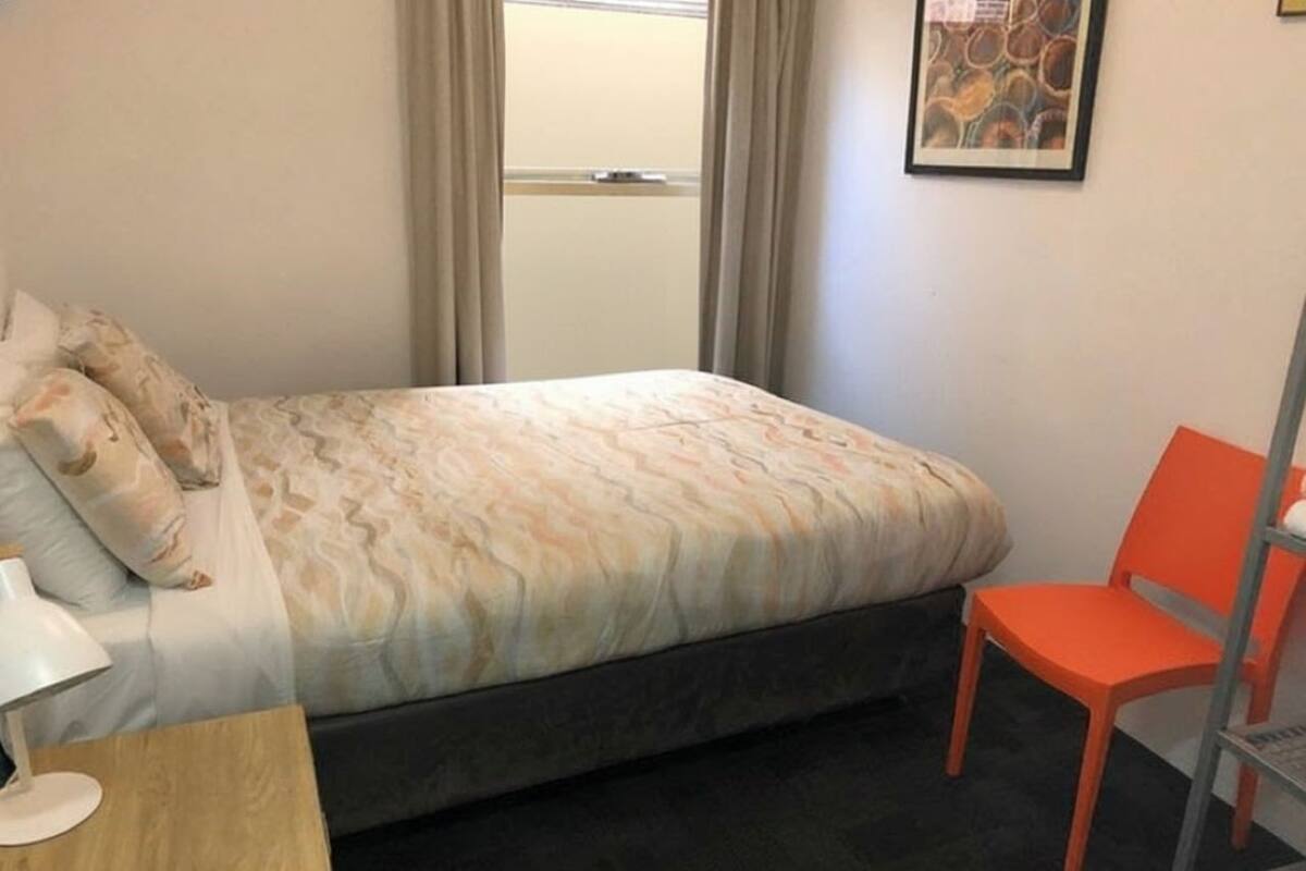Un dormitorio con una cama, una silla, un escritorio y una ventana con cortinas.
