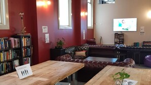 A cozy cafe with wooden tables and a leather couch, a bookshelf filled with books, and a television on the wall.