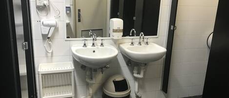 A public restroom with two sinks, a hand dryer, a paper towel dispenser, a mirror, and a trash bin.