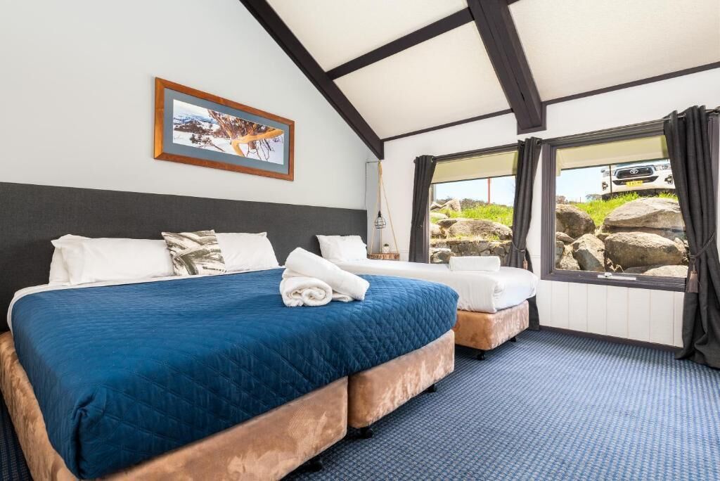 Een hotelkamer met een groot bed, een kleiner bed, een raam met uitzicht op rotsen, en een ingelijste foto aan de muur.