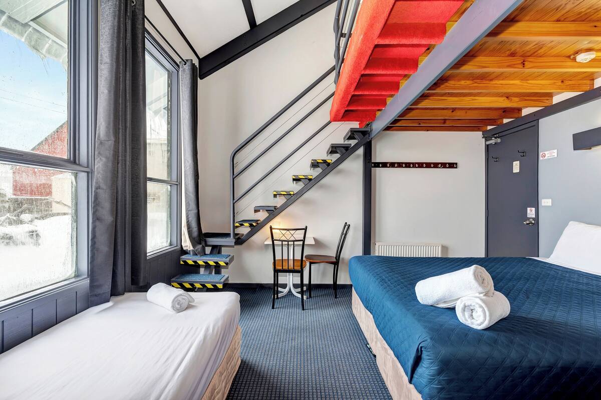 A hotel room with a bed, a desk, a chair, and a staircase.