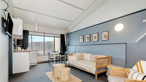 A modern room with a sofa, two round tables, a dining area, and artwork on the wall. - Snowy Gums (Smiggin Holes)
