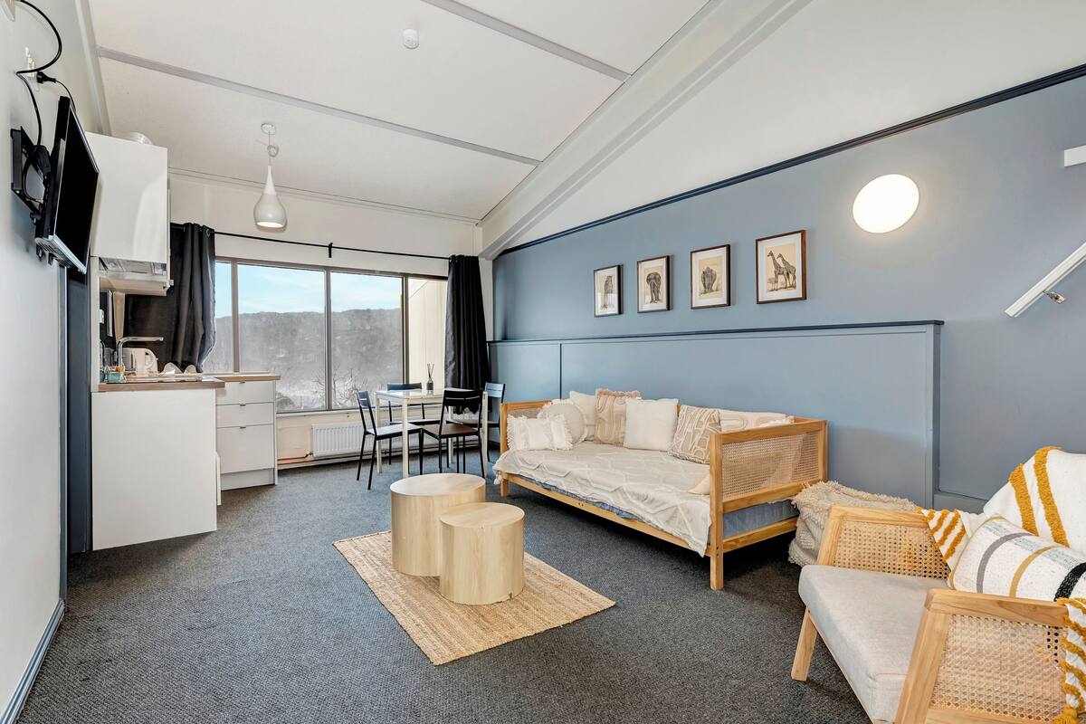 A modern room with a sofa, two round tables, a dining area, and artwork on the wall.