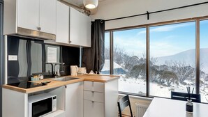 A modern kitchen with a wooden countertop, a microwave, and a view of a snowy landscape through large windows. - Snowy Gums (Smiggin Holes)