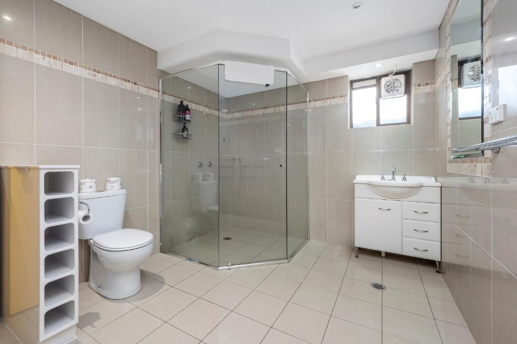 A modern bathroom with a glass-enclosed shower, a toilet, a sink, and a mirror.