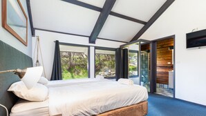 A modern bedroom with a large bed, a desk, and a view of the outdoors through large windows. - Snowy Gums (Smiggin Holes)