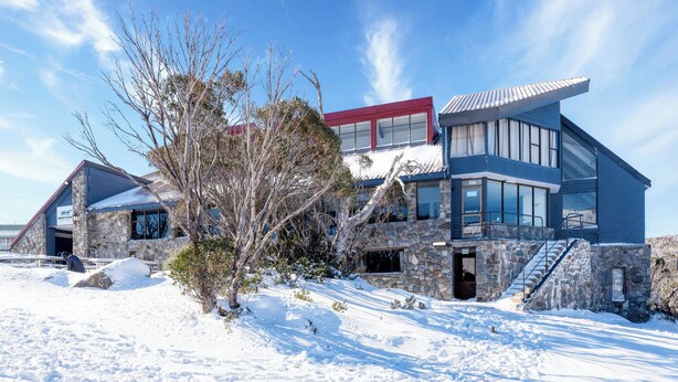 A modern two-story house with a stone facade, large windows, and a red roof. - Snowy Gums (Smiggin Holes)