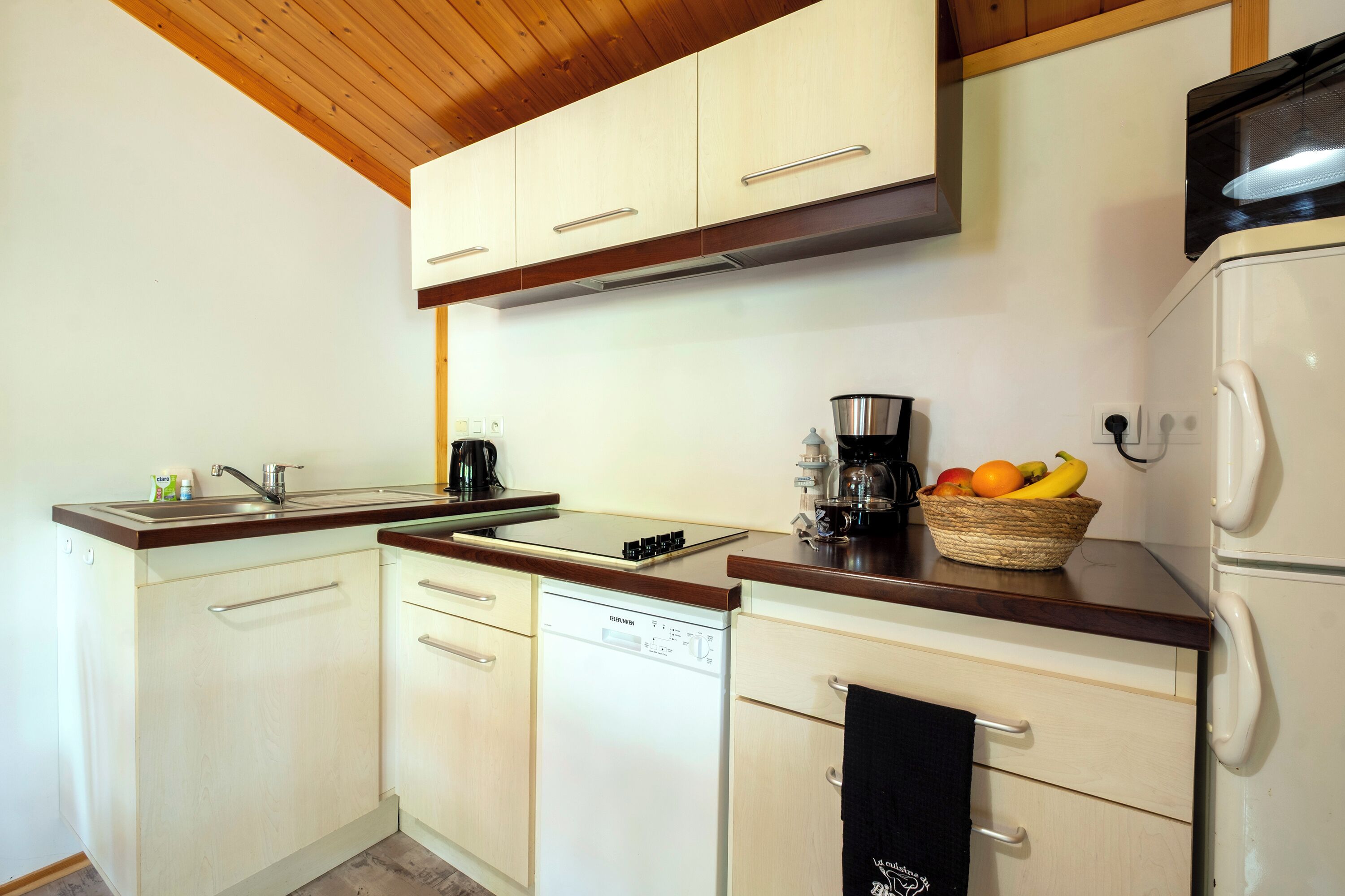A kitchen with white cabinets, a dishwasher, a microwave, and a fruit basket on the counter.
