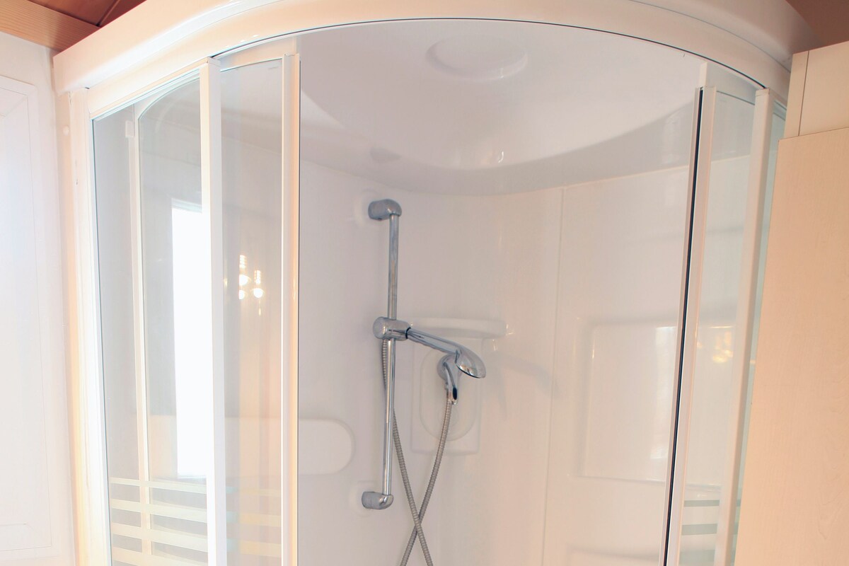 A glass-enclosed shower stall with a handheld showerhead and a wall-mounted faucet.