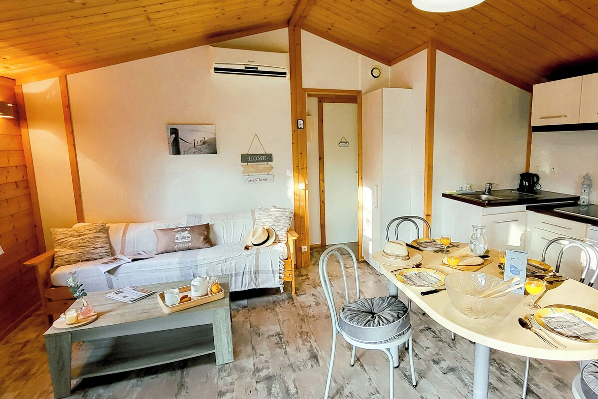 A cozy room with a wooden ceiling, a dining table set for four, a sofa with cushions, and a kitchen area with cabinets and appliances.