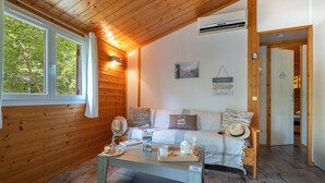 Una habitación acogedora con paredes de madera, una cama con almohadas, una mesita de noche con una bandeja y una ventana con cortinas.