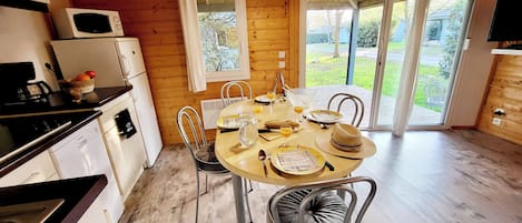 Un comedor con una mesa de madera dispuesta para dos, una cocina con electrodomésticos y vistas al exterior.