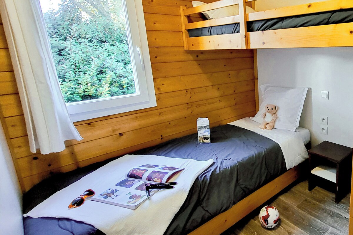 Acogedora habitación tipo cabaña con literas, una mesita de noche pequeña, una ventana con vistas a follaje y un oso de peluche en la cama.