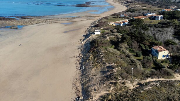 Una zona costera con una playa arenosa, algunas casas y una vista despejada del océano.