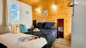 Un dormitorio acogedor con techo de madera, una cama grande con colcha azul oscuro, una ventana con cortinas y una lámpara de pared.