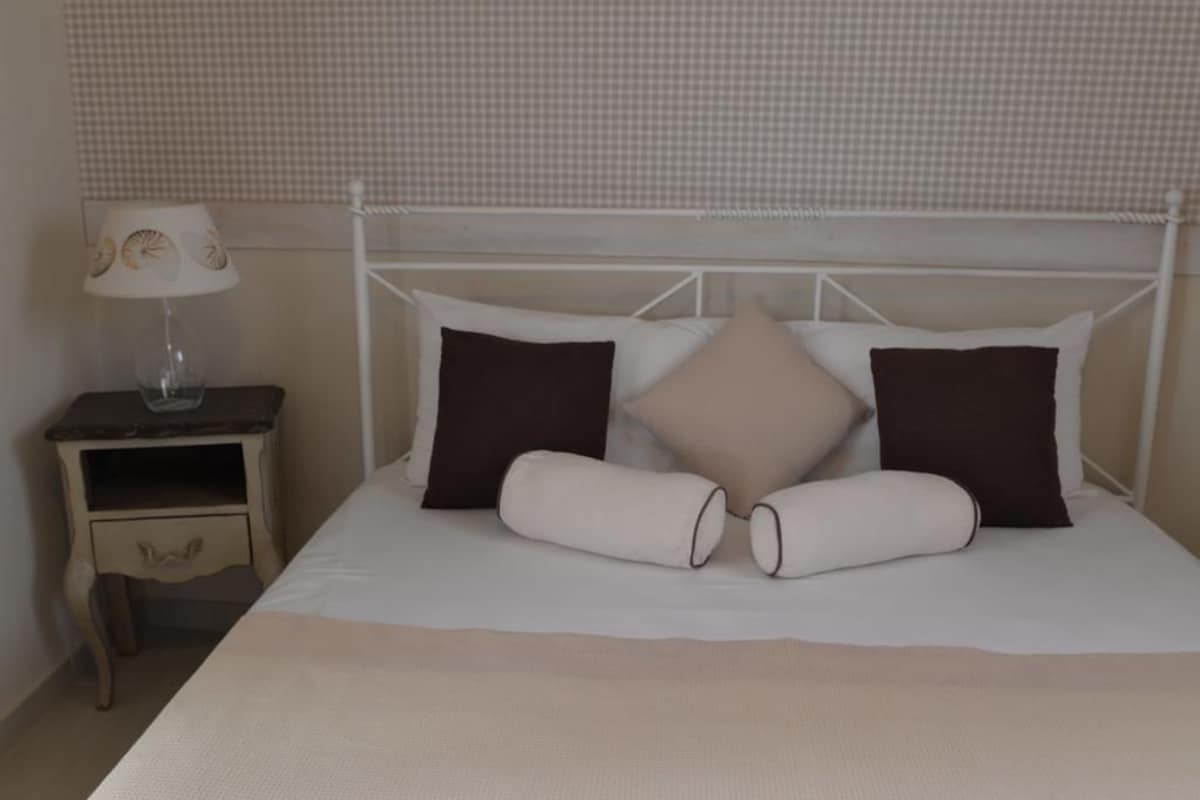 A neatly made bed with a white headboard, two pillows, and a bedside table with a lamp.