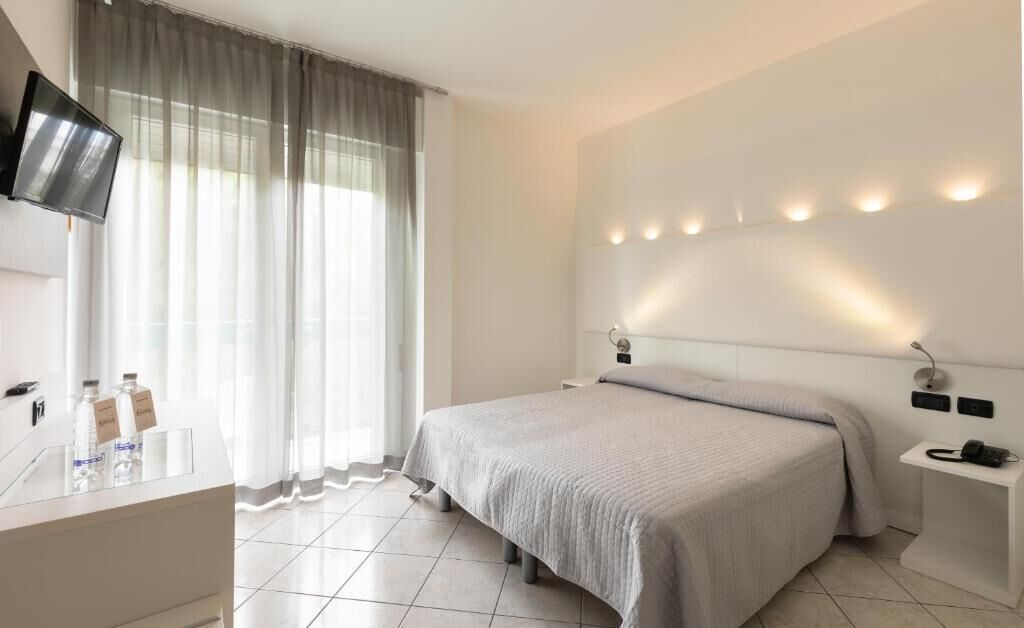 Una habitación de hotel moderna con cama, mesita de noche y televisión montada en la pared.