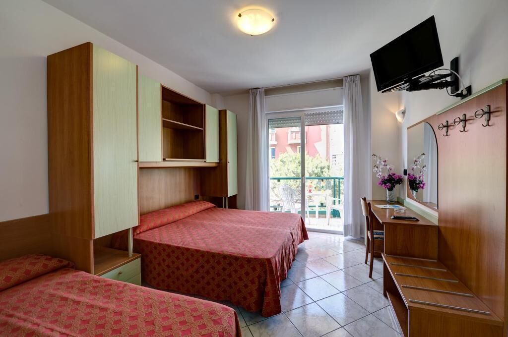 A hotel room with two beds, a desk, a TV, and a balcony with a view.