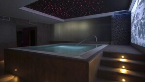 A modern spa room with a large rectangular hot tub, a staircase leading to an upper level, and a ceiling with a starry light display. - La Posada de Paco (Nijar)