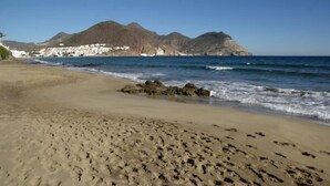 A sandy beach with footprints, a rocky outcrop, and a mountain in the background. - La Posada de Paco (Nijar)