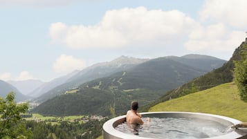 Uma pessoa em uma banheira de hidromassagem com vista para uma paisagem montanhosa.